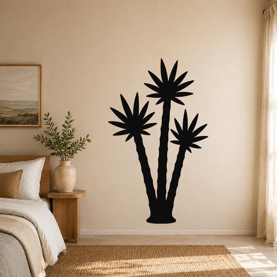Black metal wall art featuring a silhouette of three palm trees, mounted on a beige bedroom wall above a bed.