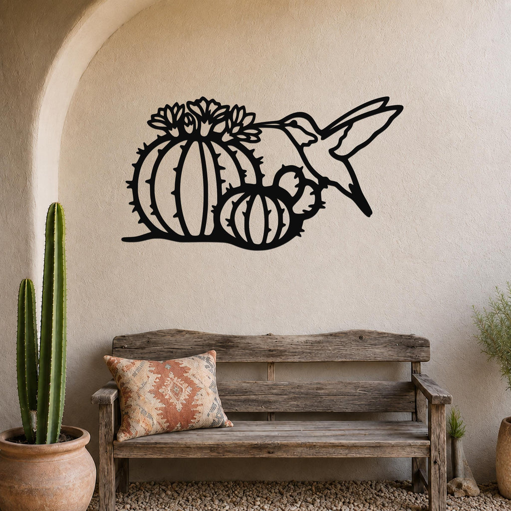 Black metal wall art featuring a hummingbird and barrel cactus with flower cutouts, mounted on a textured wall above a wooden bench in a desert-themed entryway.