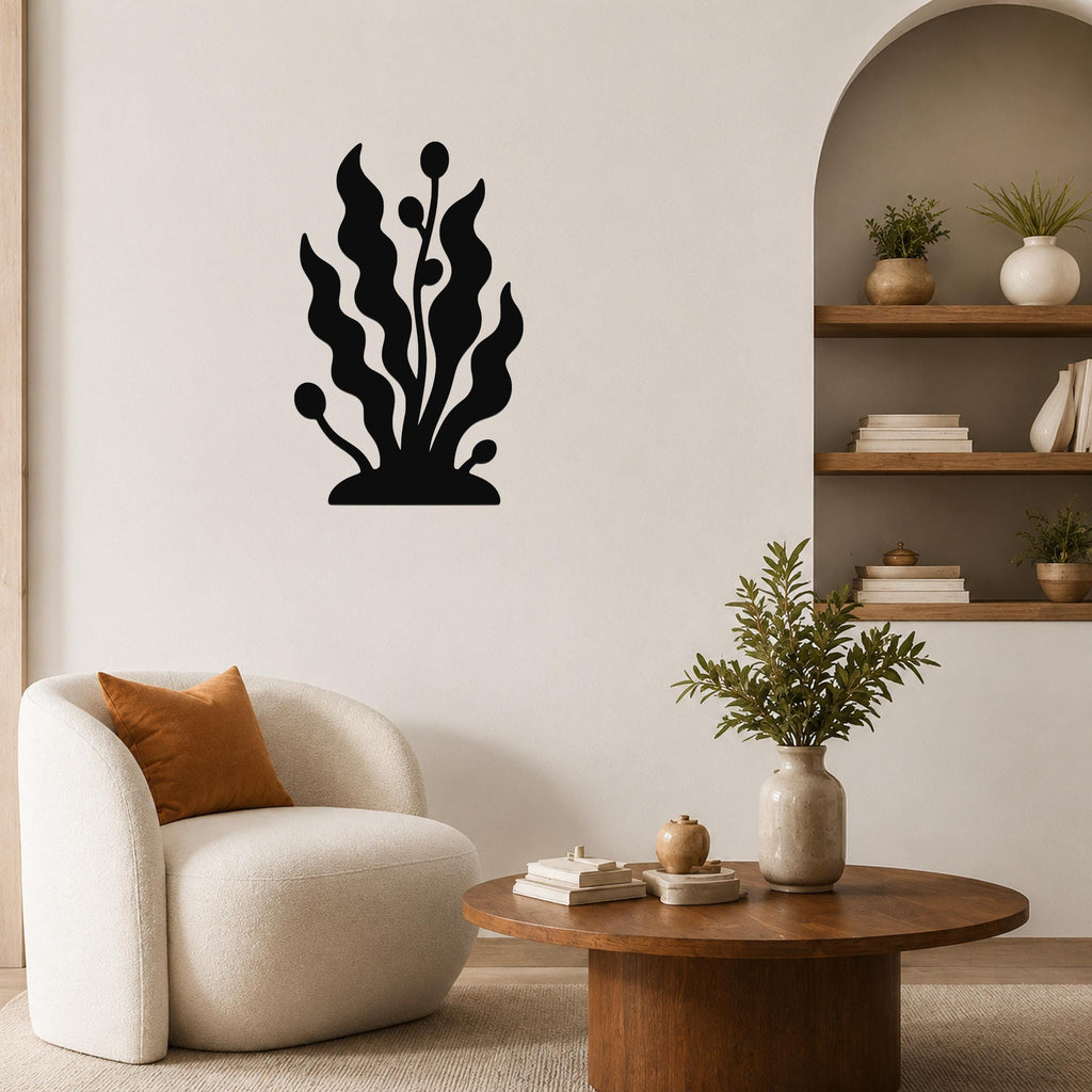 Black metal wall art in a kelp and seaweed silhouette design, mounted on a living room wall above a white armchair.