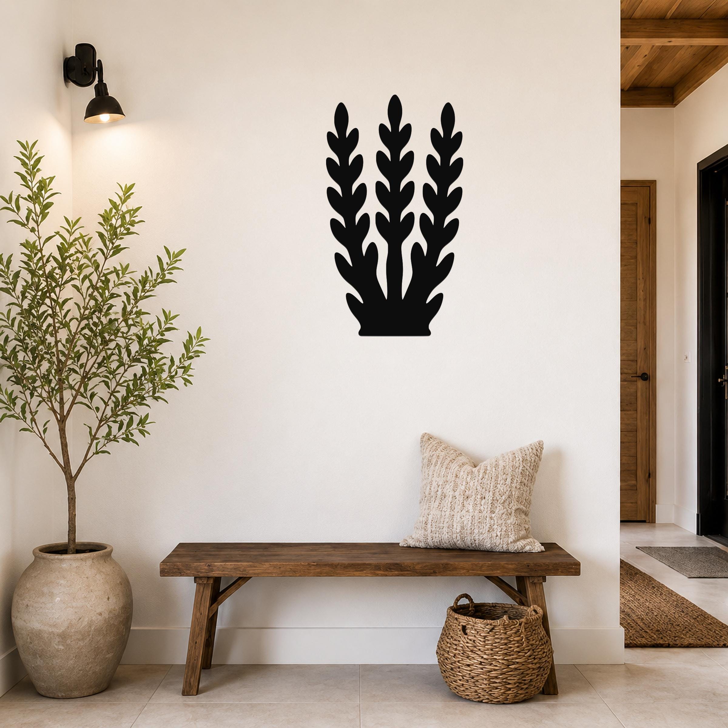 Black metal wall art with a kelp or seaweed silhouette design, mounted on a white wall above a wooden bench in an entryway.