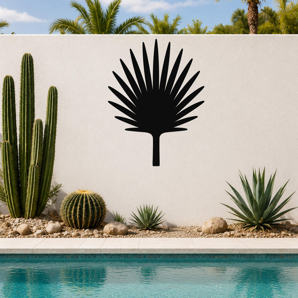 Black metal fan palm tree wall art silhouette mounted on a white outdoor wall above a pool, surrounded by cacti and succulents.