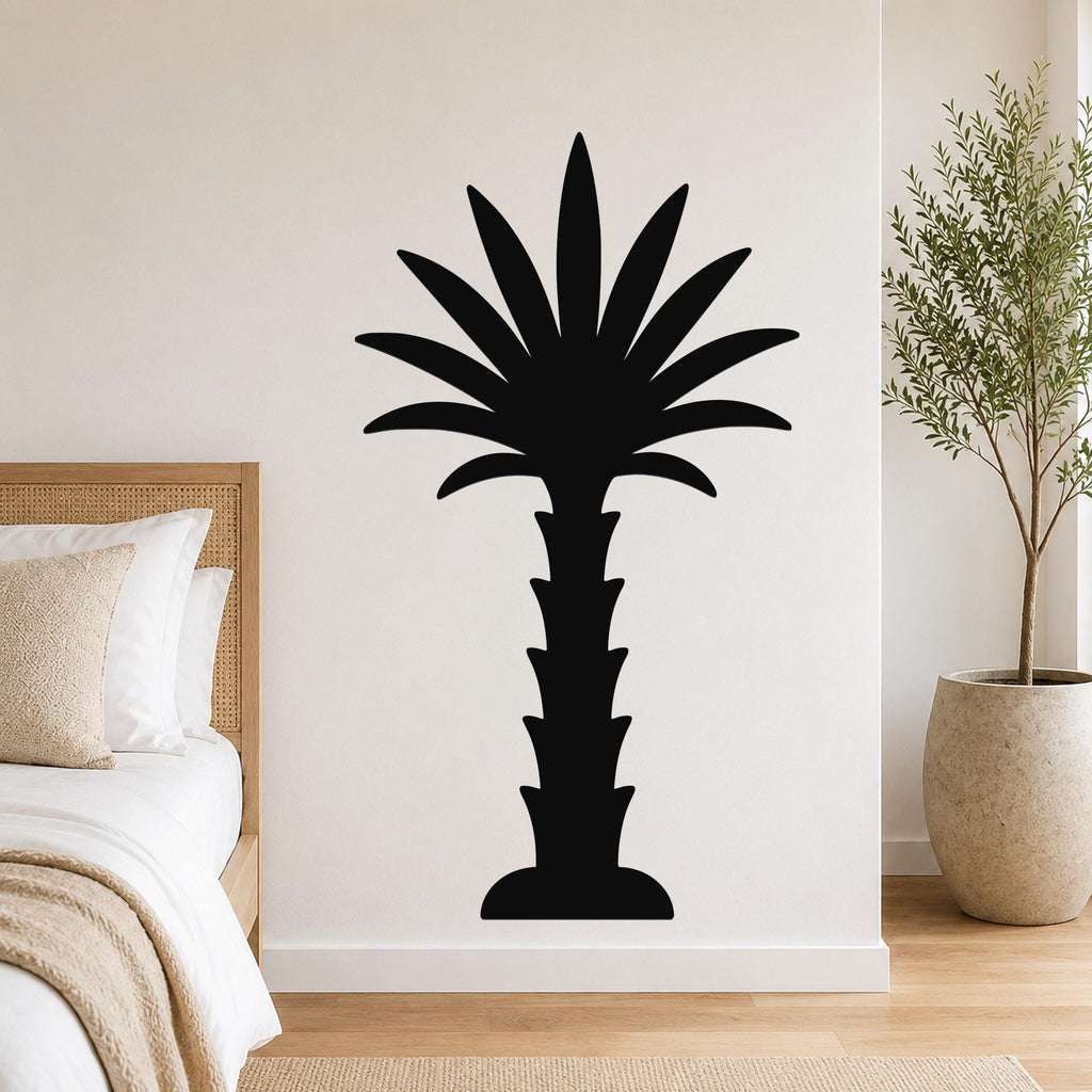 Black metal palm tree wall art silhouette mounted on a bedroom wall above a bed, with a potted plant nearby.