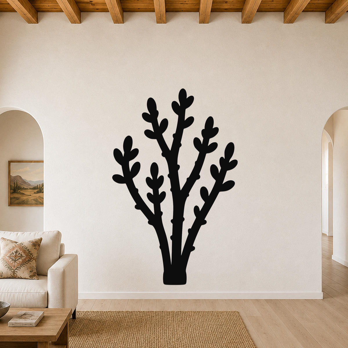 Black metal wall art in a silhouette of a desert branch with multiple spiny stems and leaf-like cutouts, mounted on a living room wall above a beige sofa.