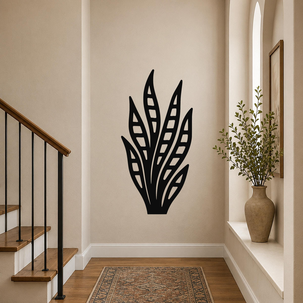 Black metal wall art in a snake plant silhouette with internal leaf cutouts, mounted on a hallway wall above a patterned rug.