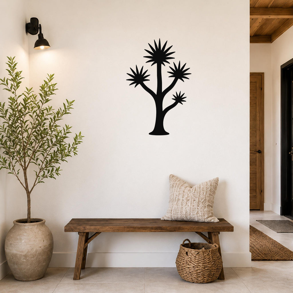 Black metal yucca wall art with starburst leaves and branching cutouts, mounted on a white wall above a wooden bench in a modern entryway.
