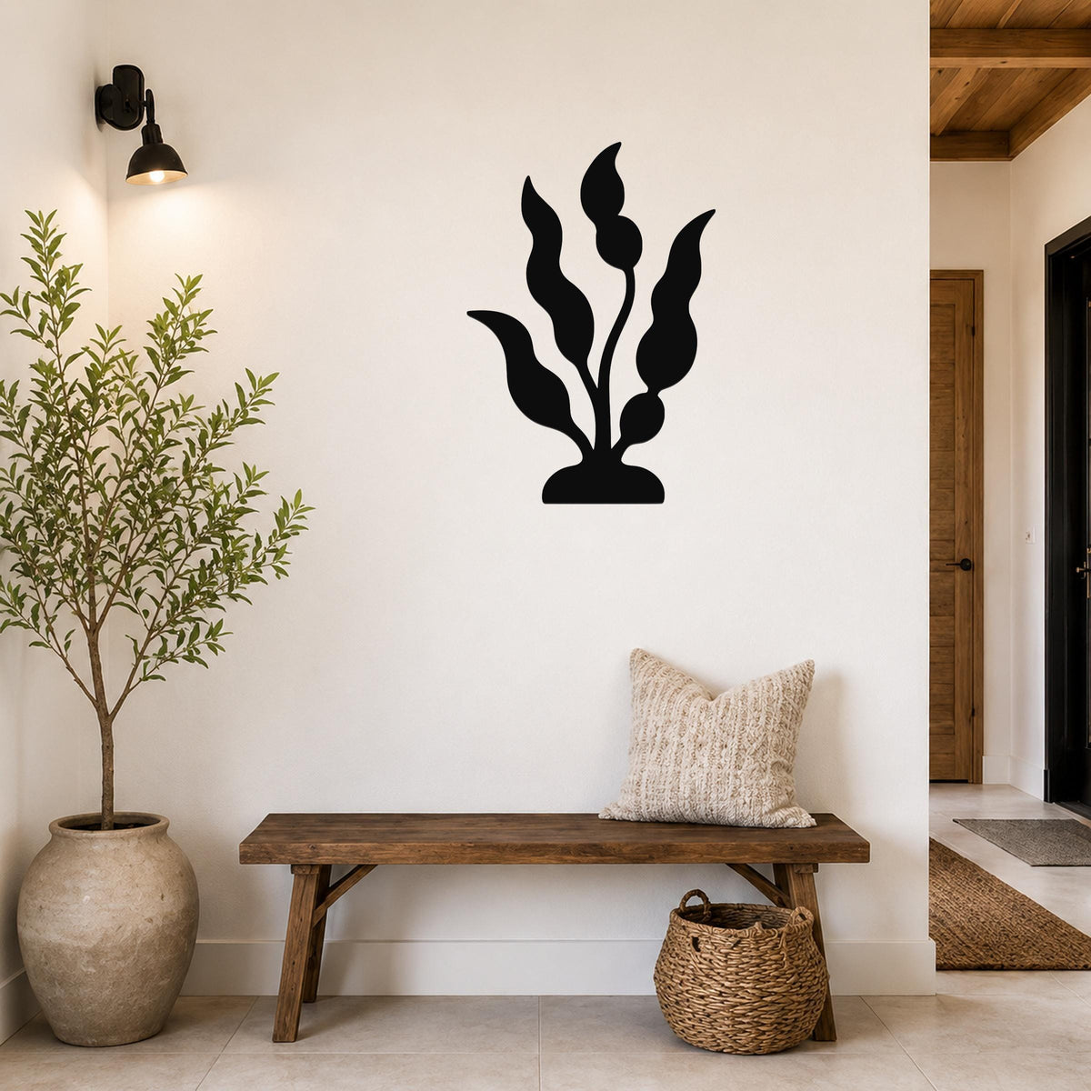 Black metal wall art cutout of a kelp or seaweed plant, mounted on a white wall above a wooden bench in a modern entryway.