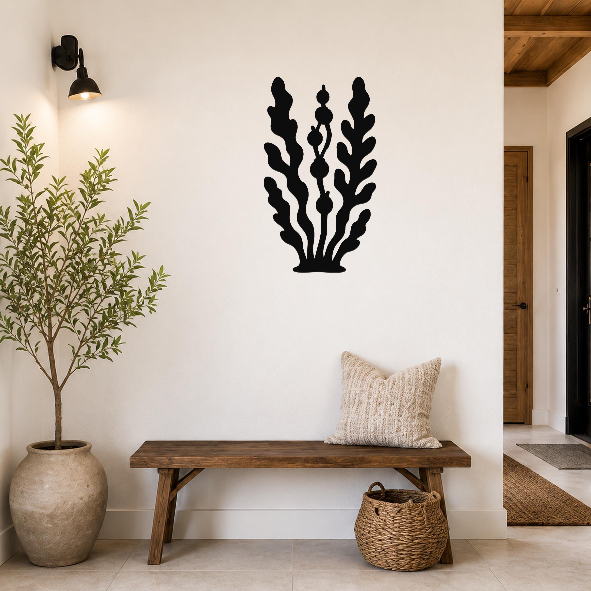 Black metal kelp and seaweed wall art with leafy fronds and bulbous cutouts, mounted on a white wall above a wooden bench in a living room.