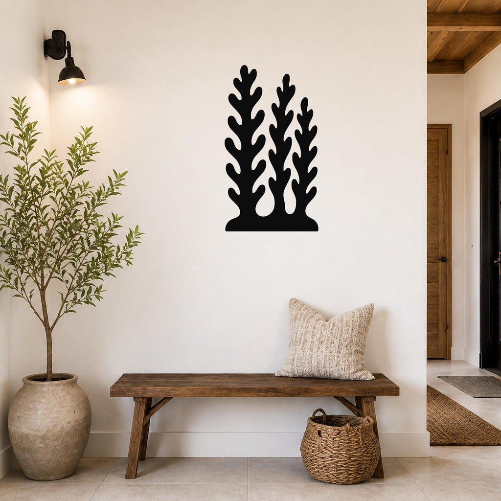 Black metal wall art with a kelp and seaweed silhouette design, mounted on a white wall above a wooden bench in a modern entryway.