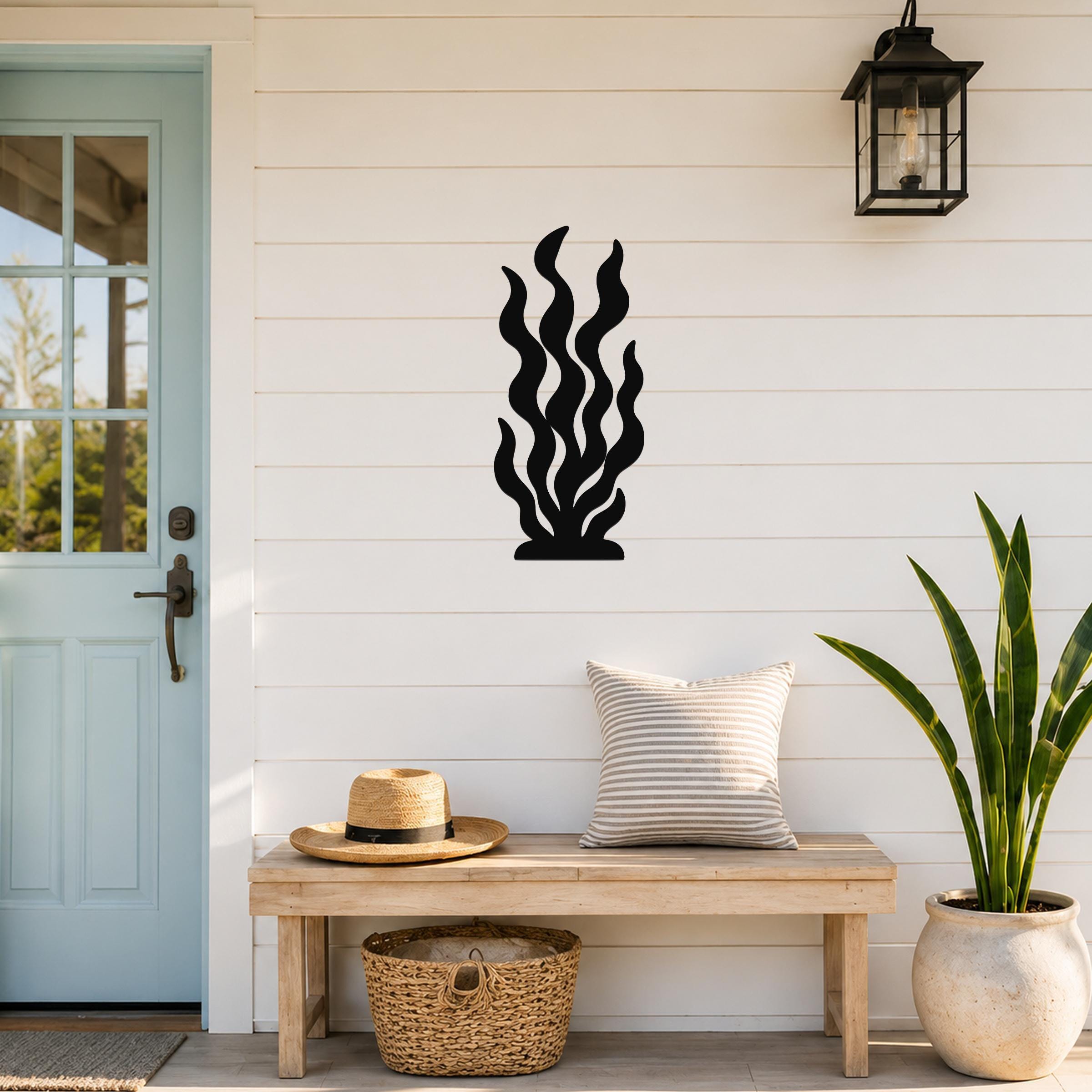 Black metal kelp wall art with wavy cutout design, mounted on a white shiplap wall above a wooden bench in a porch entryway.