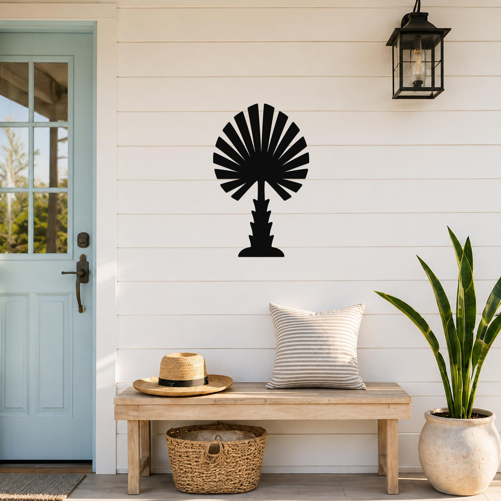 Black metal palm tree wall art with fan-shaped fronds, mounted on a white shiplap wall above a wooden bench on a porch.