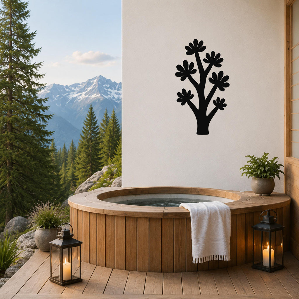Black metal wall art in a tree silhouette with flower cutouts, mounted on a white wall above a wooden hot tub on a mountain-view deck.
