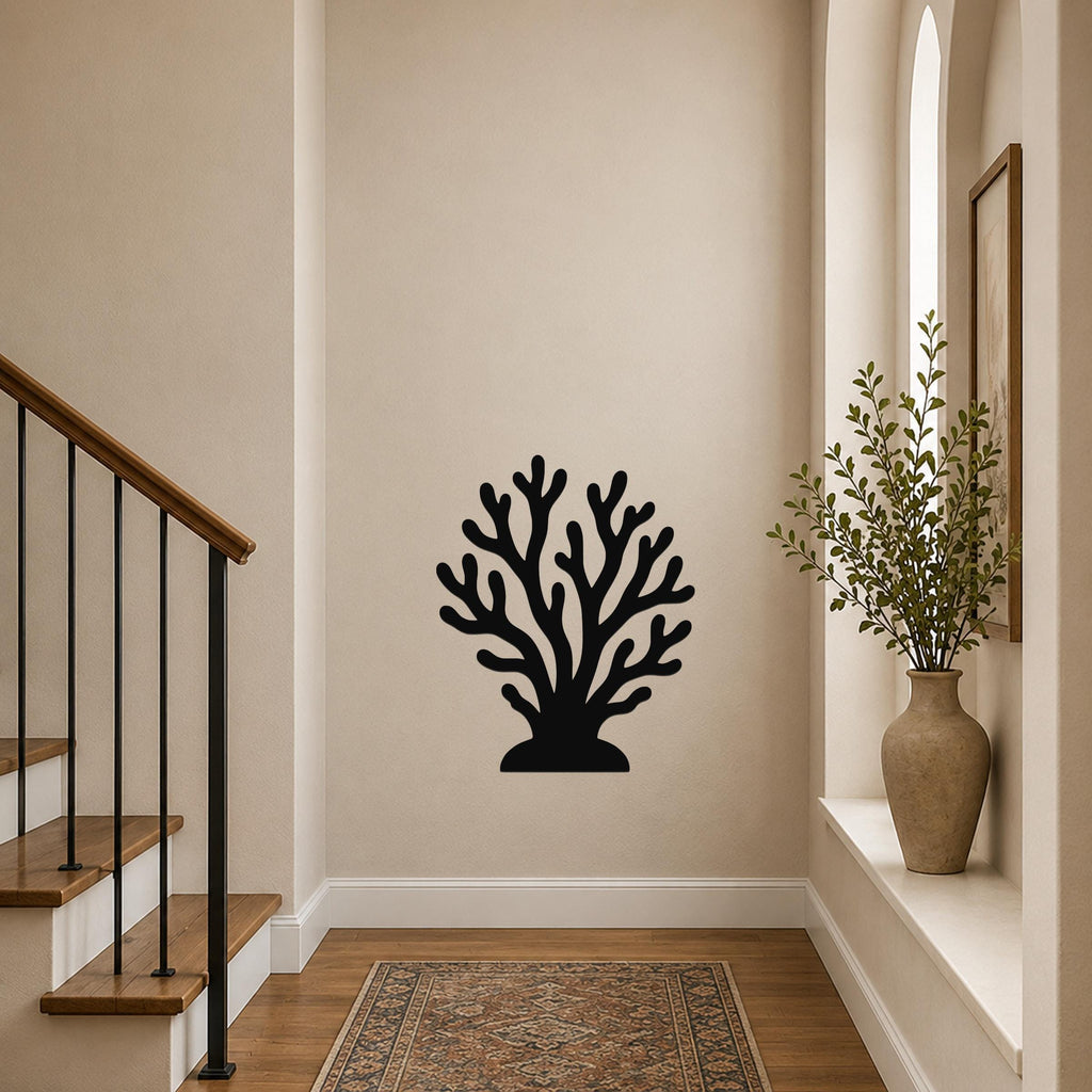 Black metal coral wall art with branching cutouts, mounted on a beige hallway wall near a staircase and a potted plant.