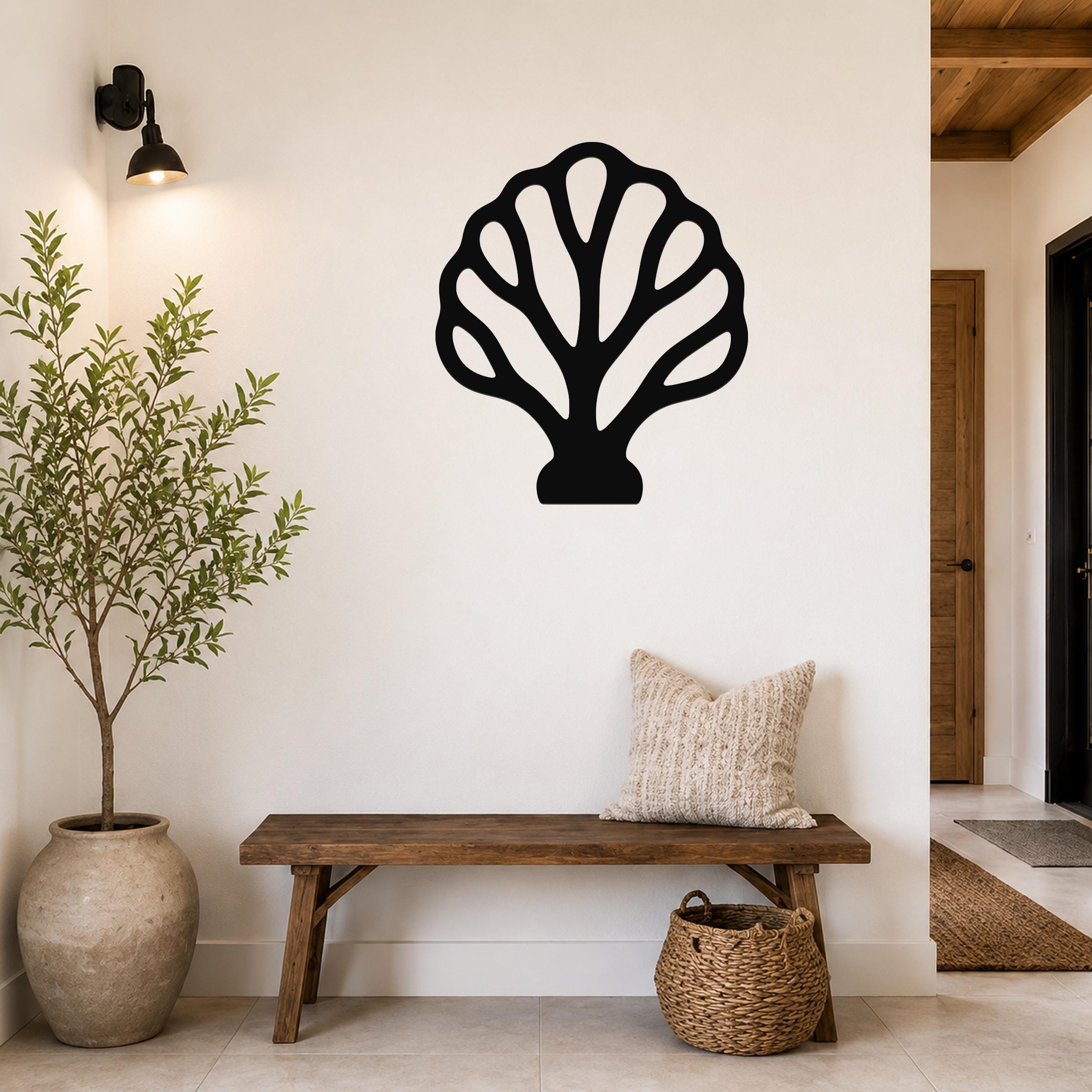 Black metal wall art in a fan coral silhouette with internal cutouts, mounted on a white wall above a wooden bench in a coastal entryway.