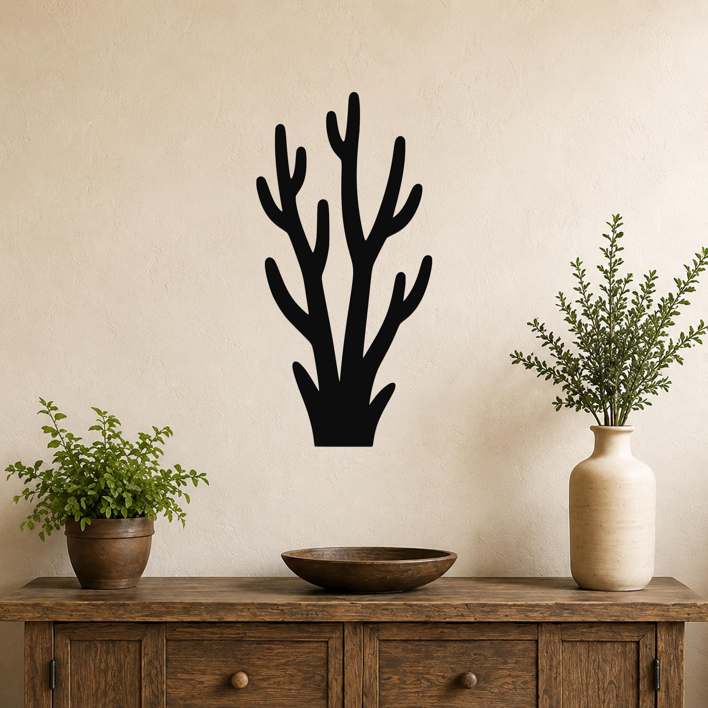 Black metal wall art in a branch silhouette design, mounted on a beige wall above a wooden console table with potted plants.