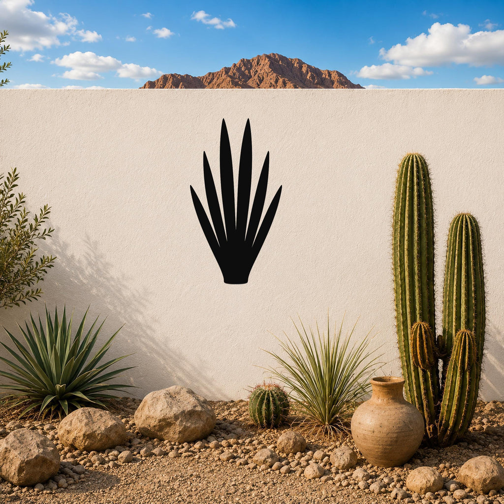 Black metal yucca wall art silhouette mounted on a white outdoor wall above a desert garden with cacti and rocks.