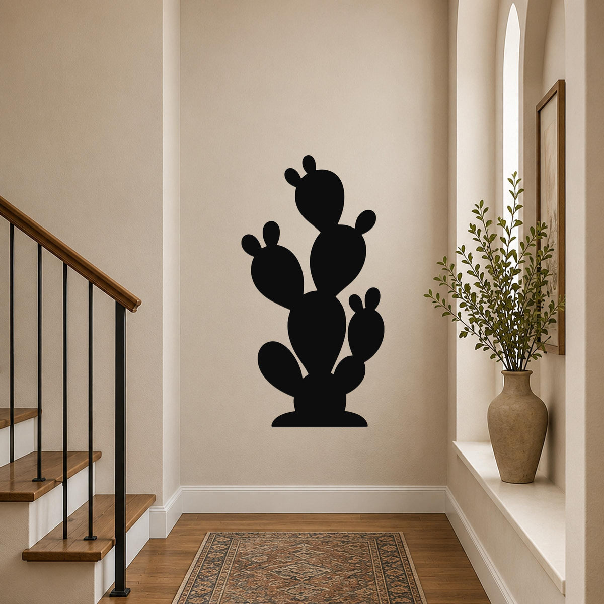 Black metal cactus wall art with a silhouette design, mounted on a hallway wall above a patterned rug near a staircase.