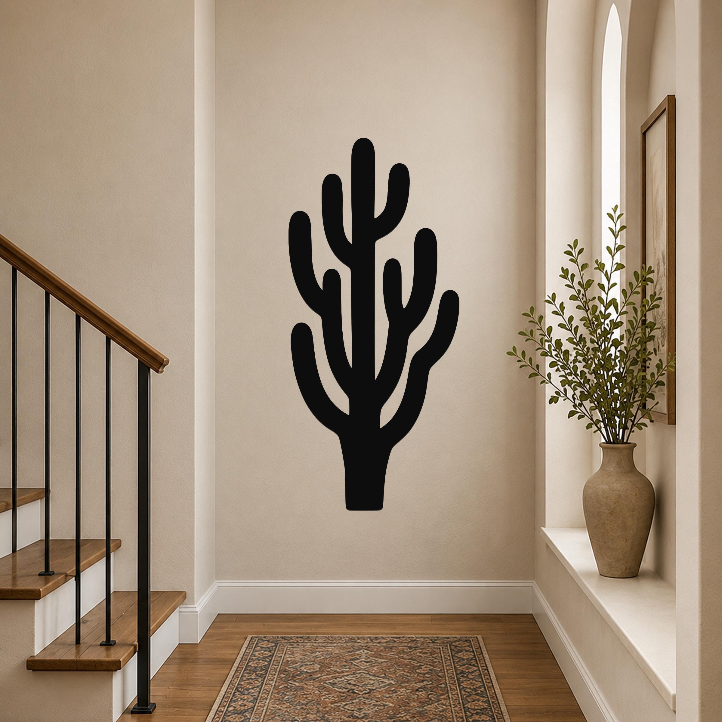 Black metal saguaro cactus wall art with branching cutouts, mounted on a hallway wall above a patterned rug.