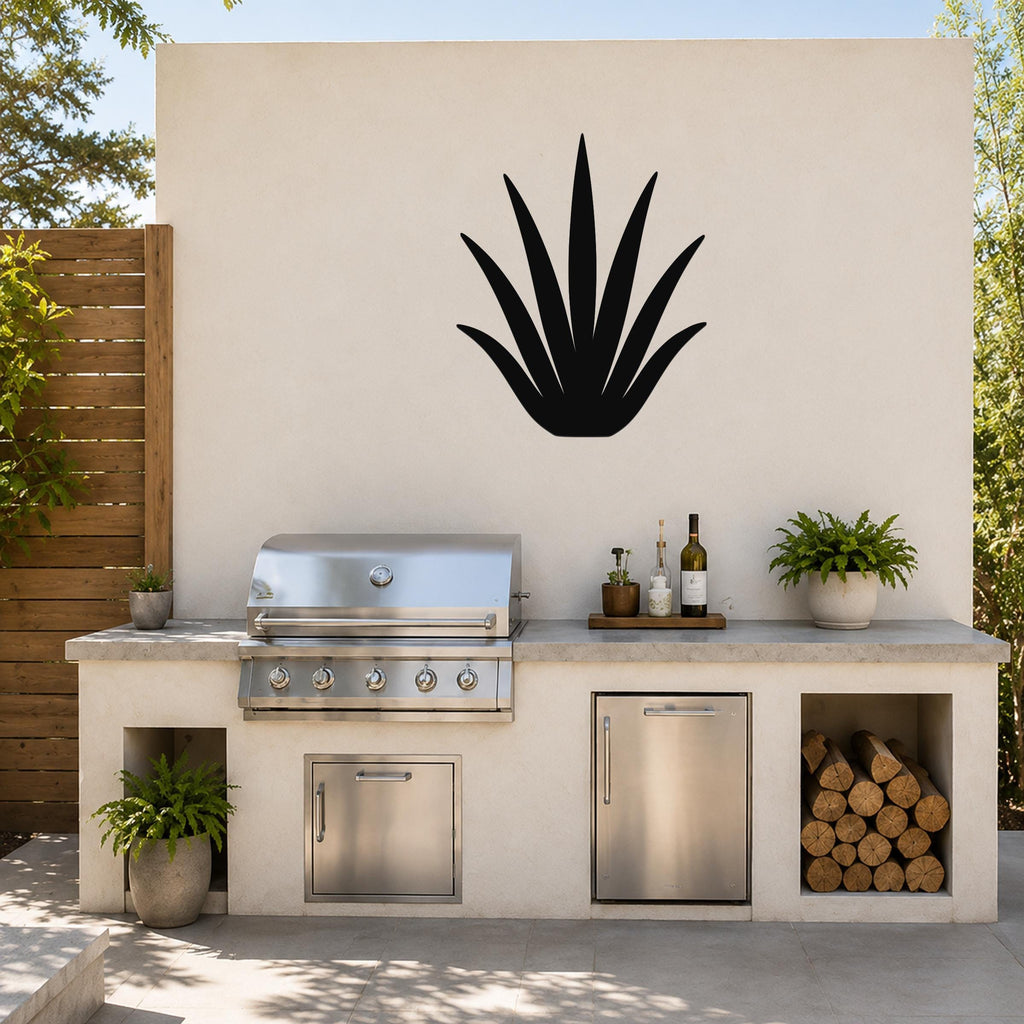 Black metal agave wall art silhouette mounted on a beige outdoor kitchen wall above a stainless steel grill and countertop.