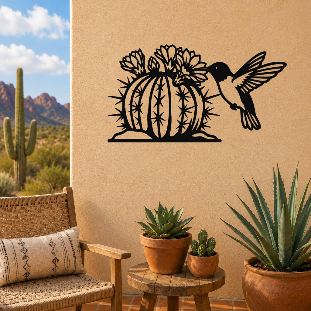 Black metal wall art featuring a hummingbird and flowering barrel cactus cutout, mounted on a tan outdoor wall above a small wooden table with potted succulents.