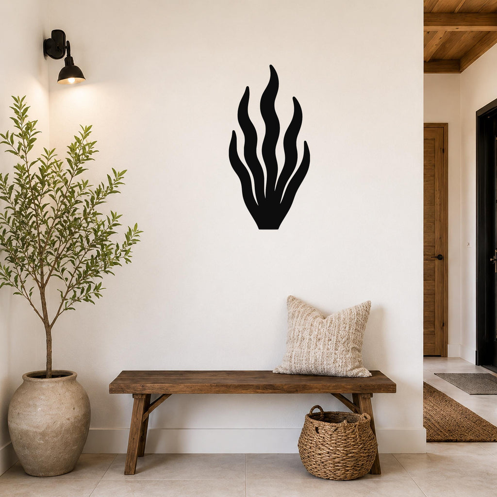 Black metal kelp wall art with flowing leaf cutouts, mounted on a white wall above a wooden bench in a coastal entryway.