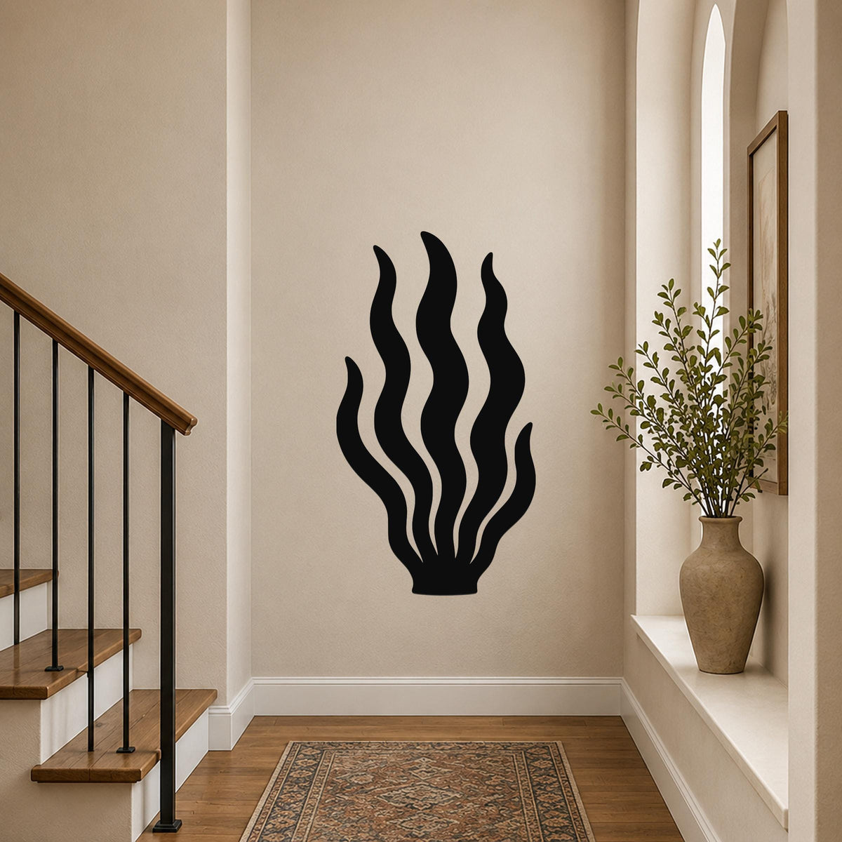 Black metal kelp wall art with flowing wavy cutouts, mounted on a hallway wall above a patterned rug near a staircase.