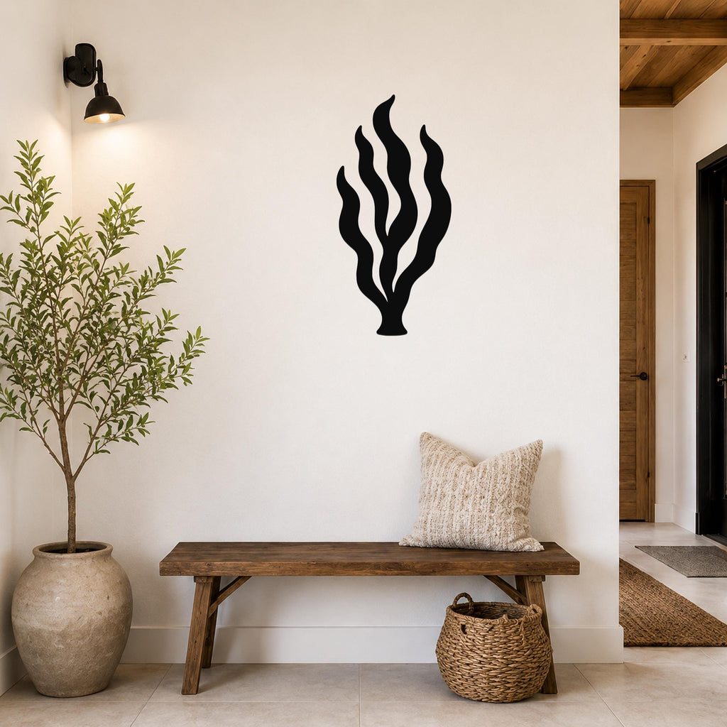 Black metal kelp seaweed wall art with flowing frond cutouts, mounted on a white wall above a wooden bench in a coastal entryway.