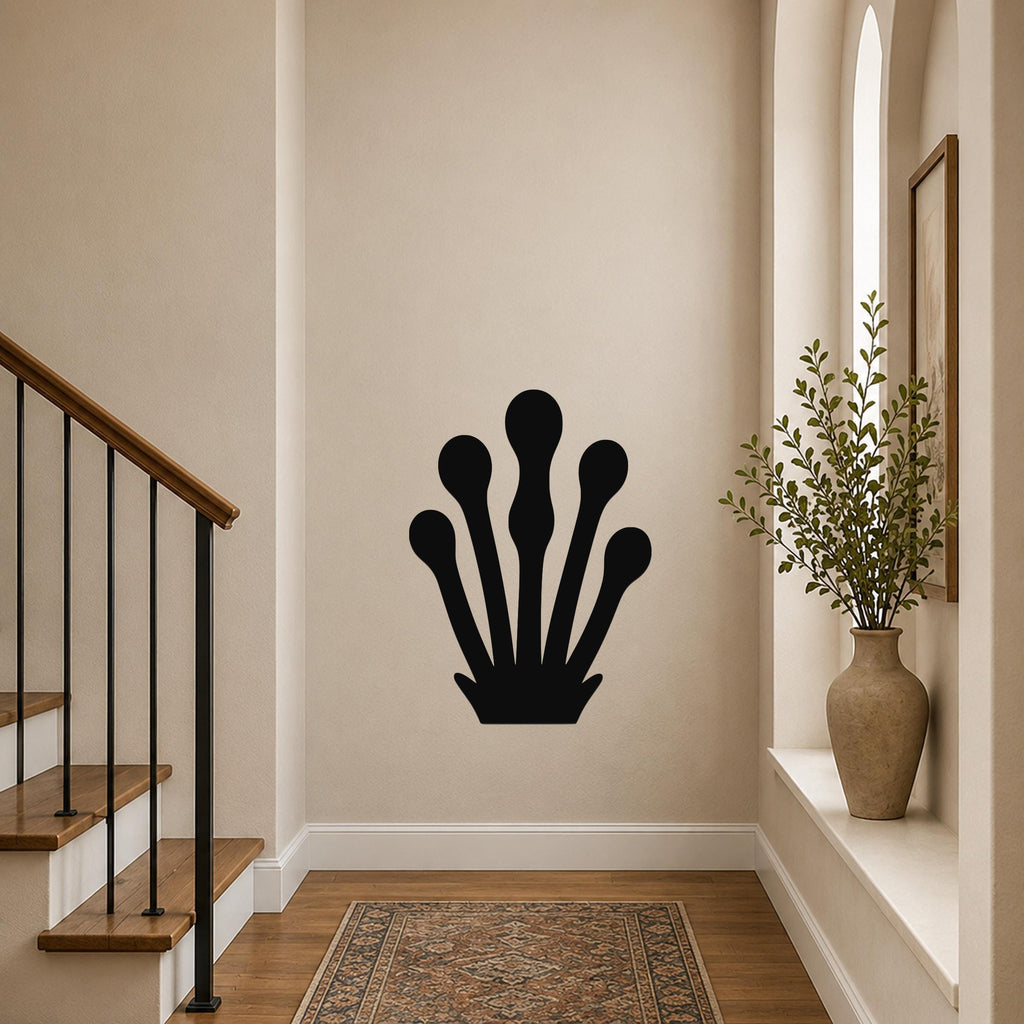 Black metal wall art in a kelp or seaweed silhouette design, mounted on a hallway wall above a patterned rug near a staircase.
