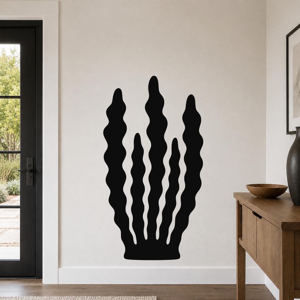 Black metal wall art with a kelp and seaweed silhouette design, mounted on a living room wall above a wooden console table.