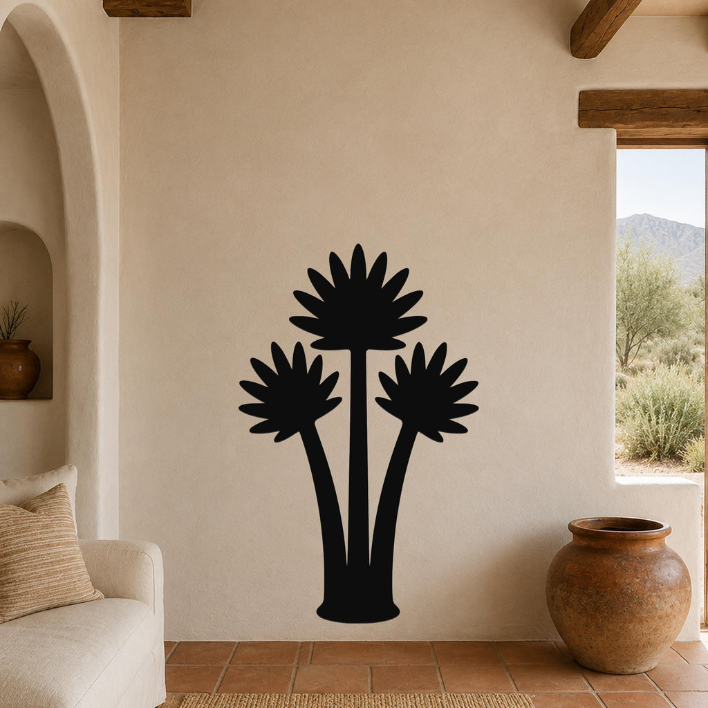 Black metal wall art silhouette of three fan palm trees, mounted on a beige stucco wall in a living room with terracotta tile flooring.