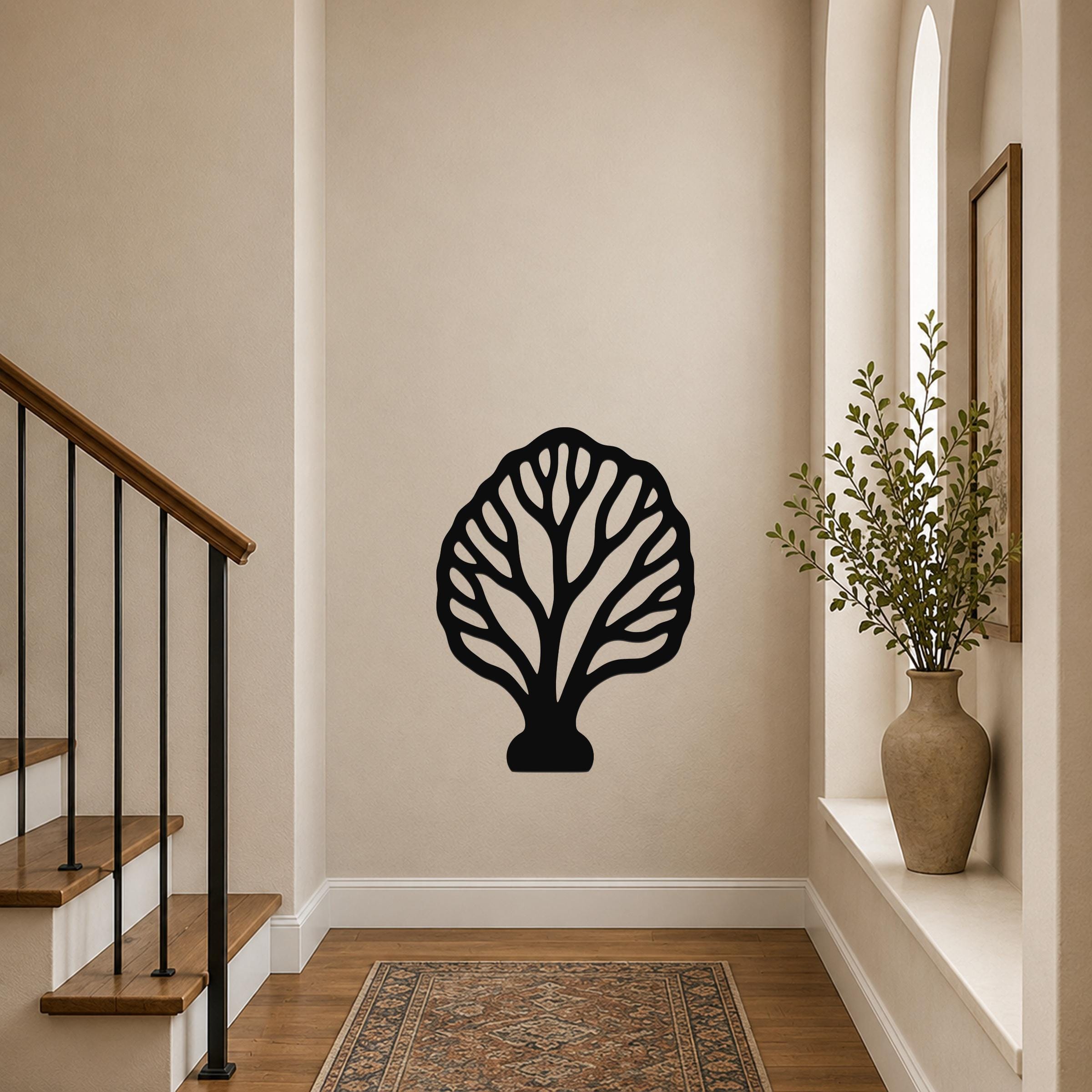 Black metal wall art in a fan coral silhouette with intricate internal cutouts, mounted on a beige hallway wall near a staircase and a potted plant.