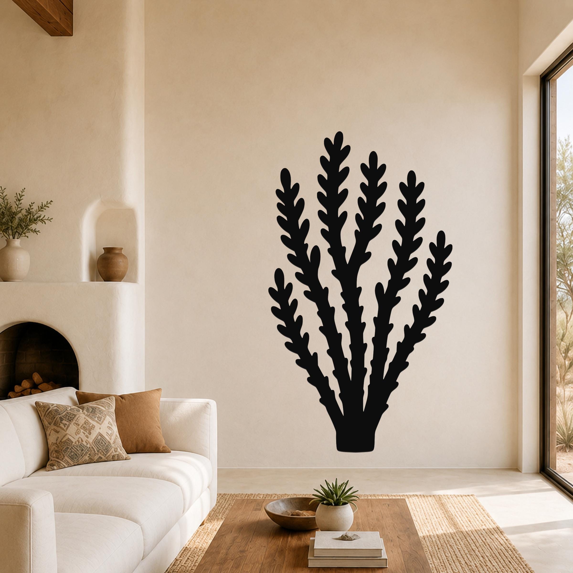 Black metal wall art in a branching desert plant silhouette, mounted on a living room wall above a white sofa.