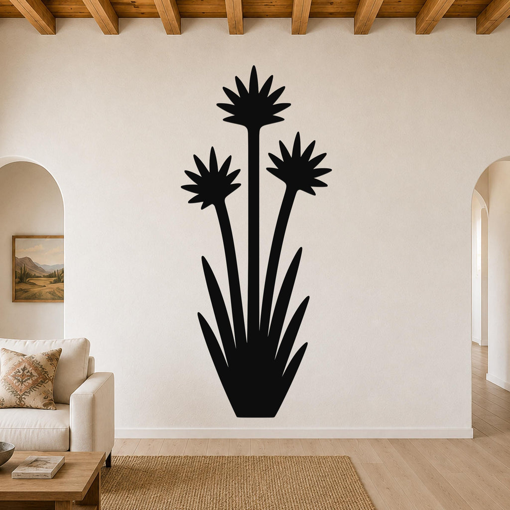 Black metal yucca wall art with three blooming flower silhouettes and long leaves, mounted on a living room wall above a sofa.