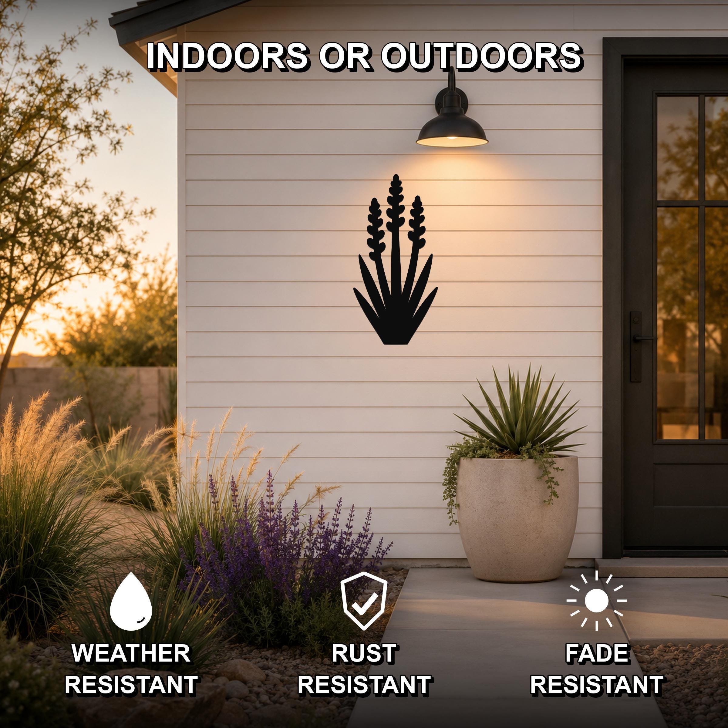 Black metal yucca wall art with layered leaf cutouts, mounted on a white shiplap exterior wall above a patio, illuminated by a wall sconce.