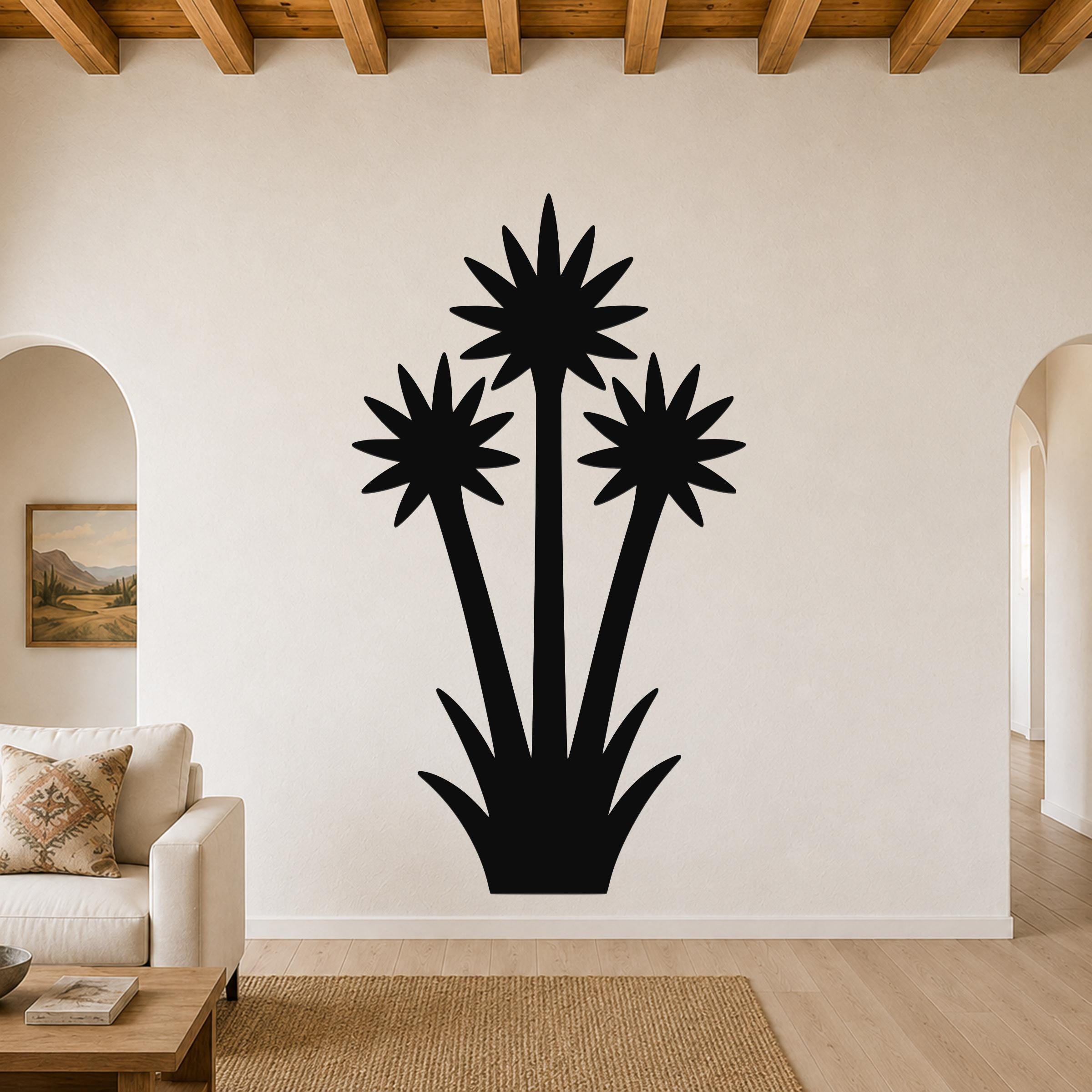 Black metal wall art silhouette of a blooming yucca plant with three starburst-like flower heads and spiky base, mounted on a living room wall above a sofa.