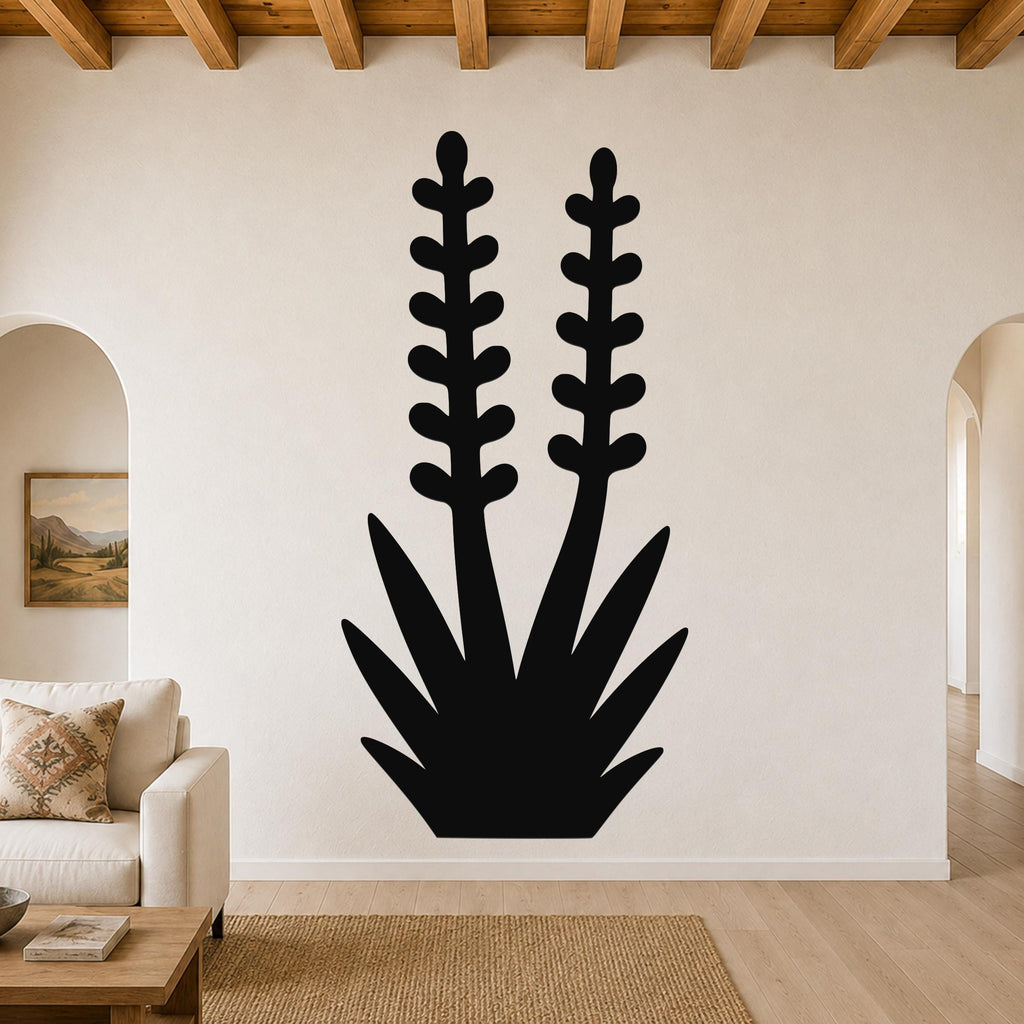 Black metal wall art in the silhouette of a blooming yucca plant with two tall flower stalks and spiky leaves, mounted on a living room wall above a sofa.