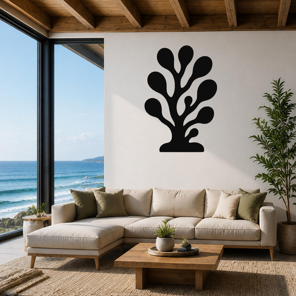Black metal coral wall art with organic branching cutouts, mounted on a white wall above a beige sectional sofa in a living room with ocean views.