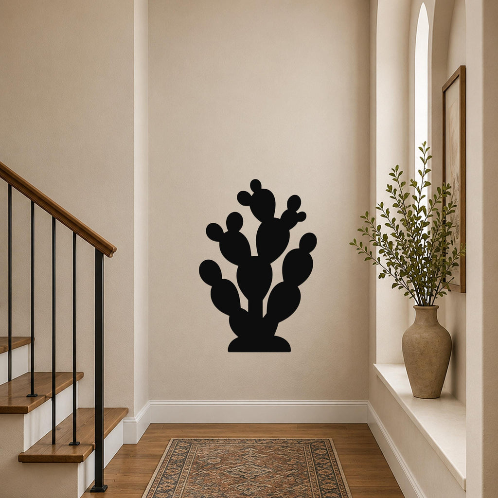 Black metal prickly pear cactus wall art with layered pads and cutout details, mounted on a hallway wall above a patterned rug near a staircase.