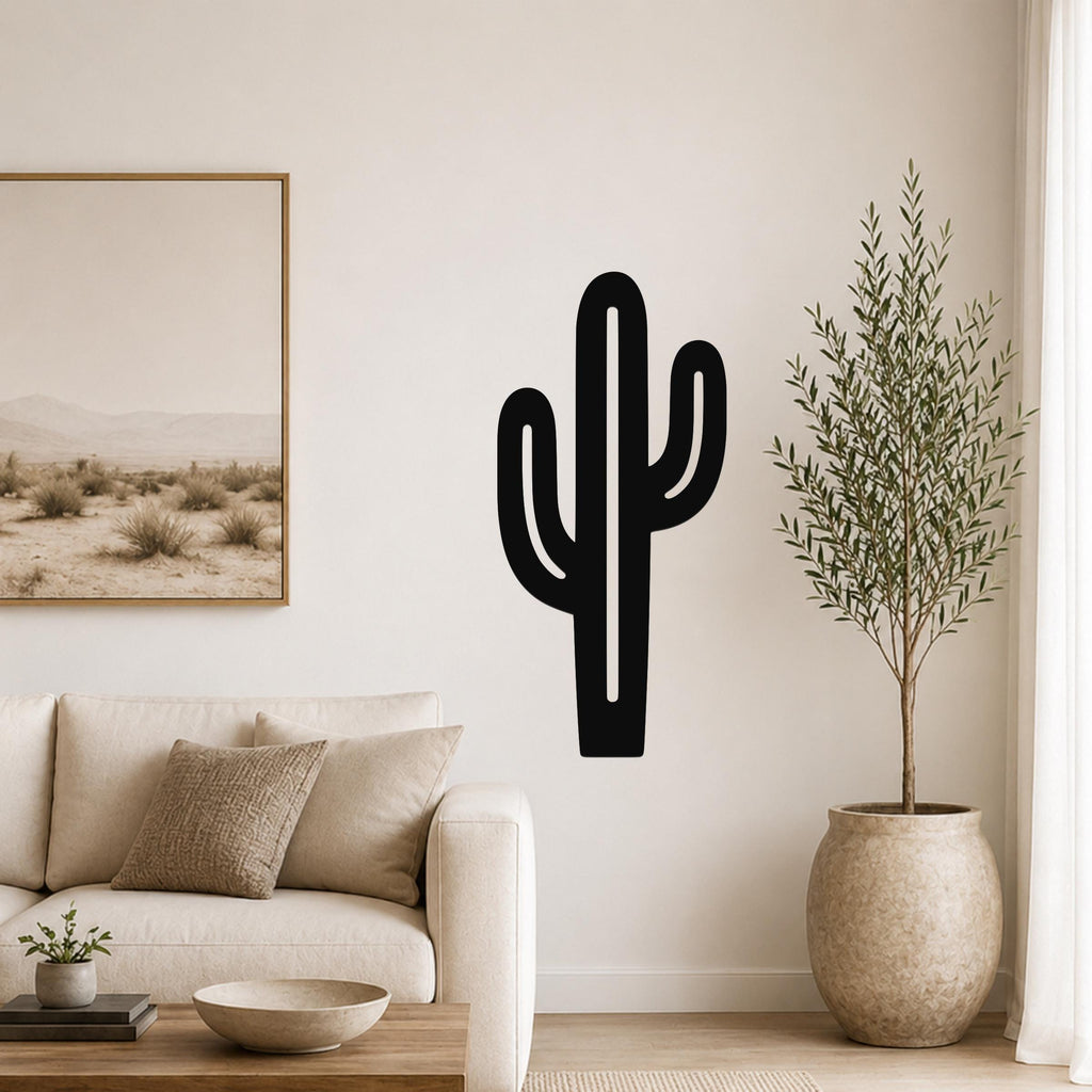 Black metal saguaro cactus wall art with cutout arms, mounted on a living room wall above a beige sofa.