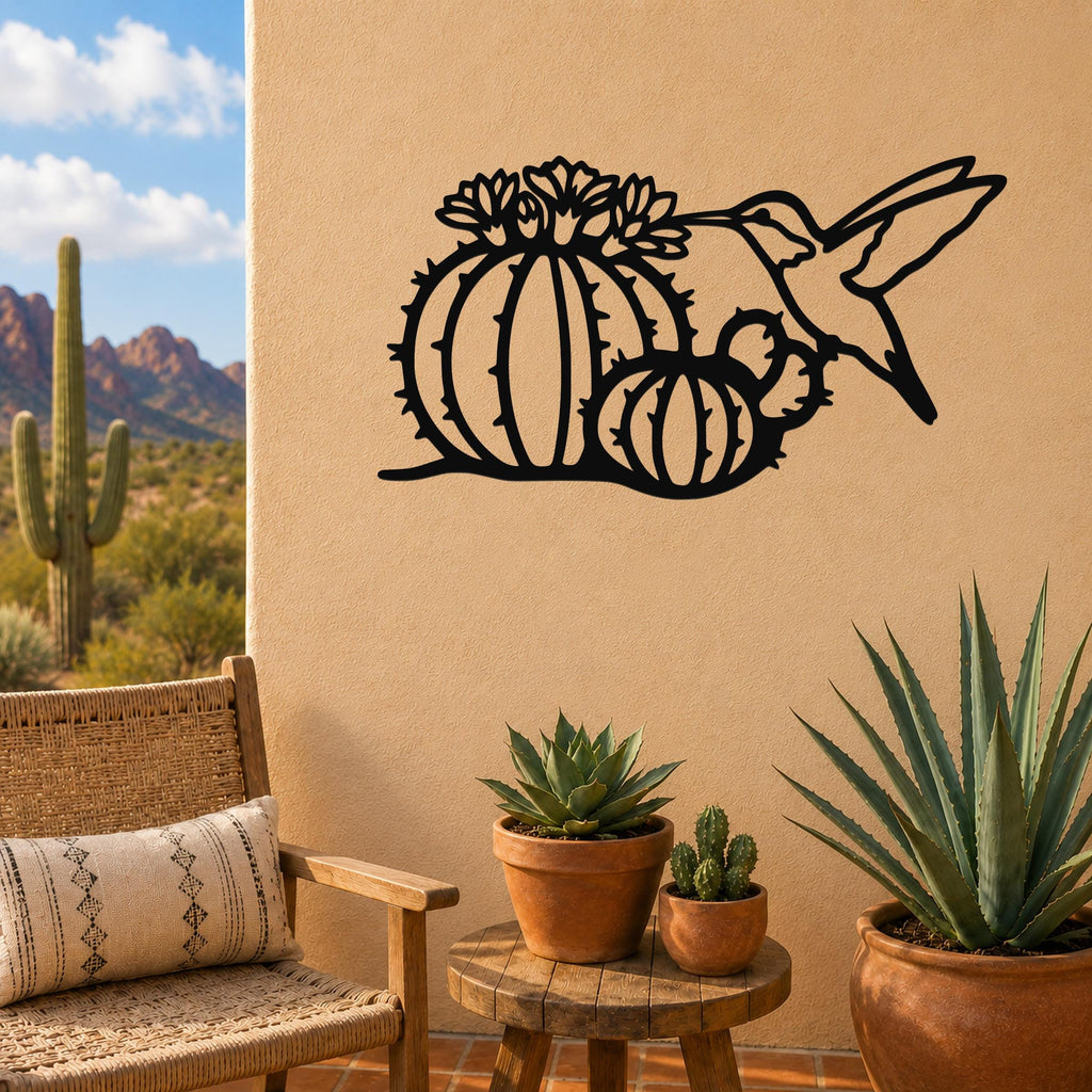 Black metal wall art featuring a hummingbird and barrel cactus with flower cutouts, mounted on a tan outdoor wall above a small wooden table with potted succulents.