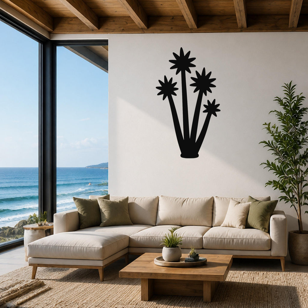 Black metal wall art silhouette of a tall yucca plant with star-shaped flower cutouts, mounted on a white wall above a beige sofa in a living room with ocean views.