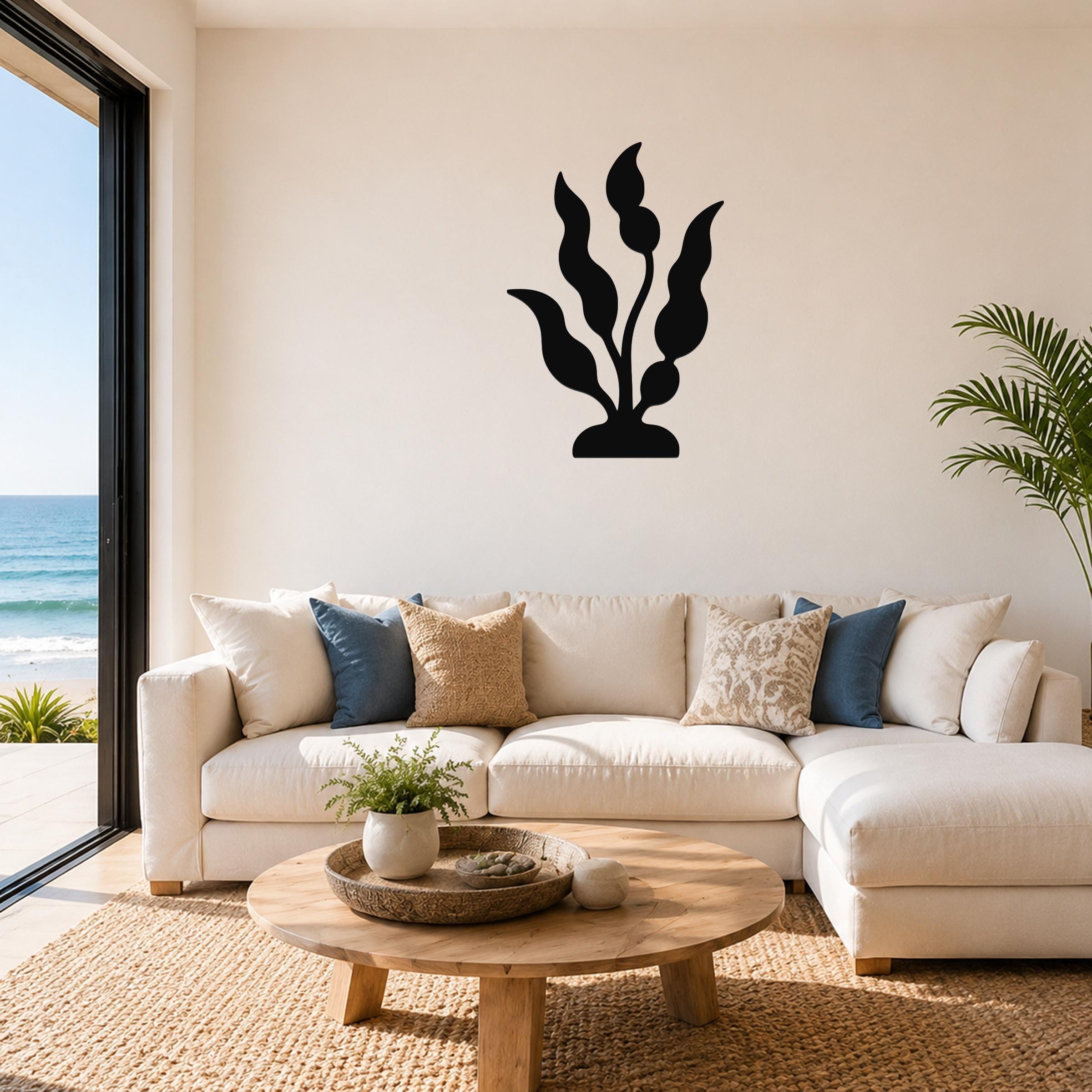 Black metal kelp wall art with flowing leaf cutouts, mounted above a white sofa in a bright living room with ocean views.