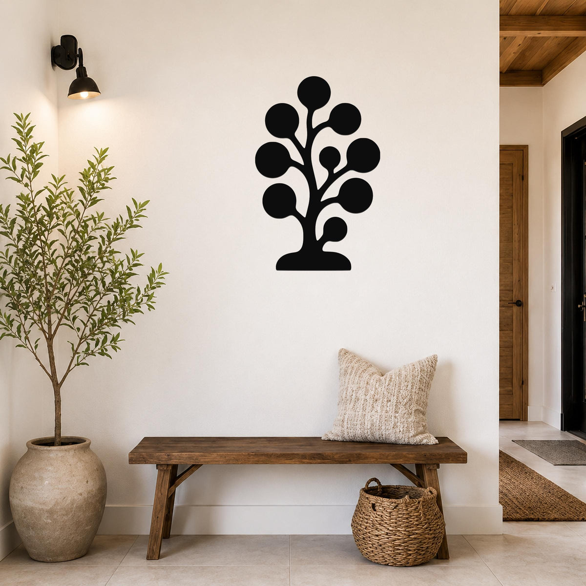Black metal wall art in a tree silhouette with circular leaf cutouts, mounted on a white wall above a wooden bench in a hallway.