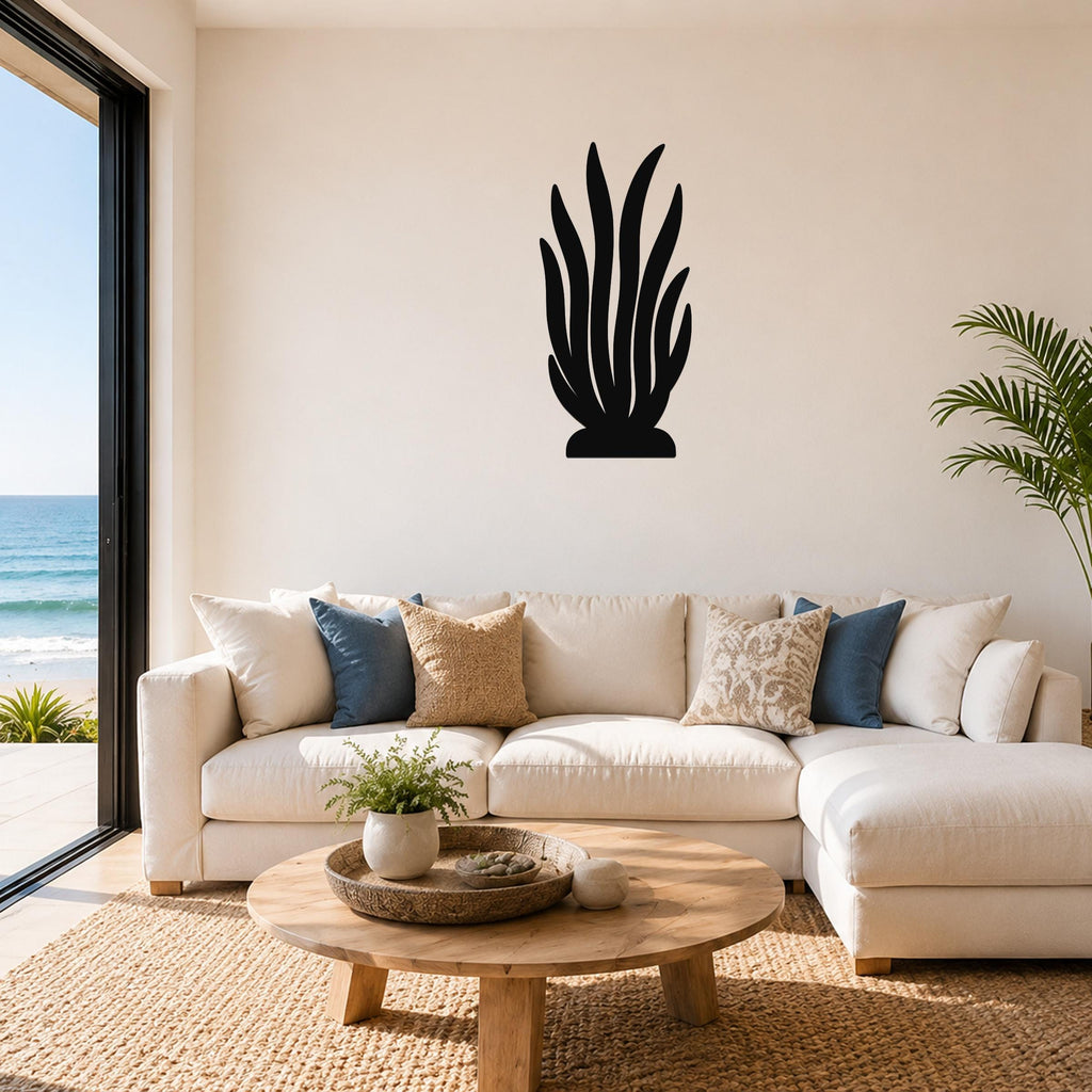 Black metal kelp wall art silhouette mounted above a white sofa in a living room with ocean views.