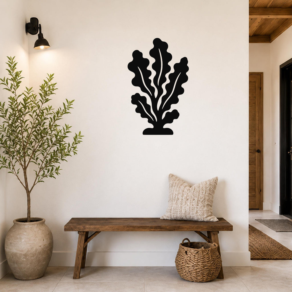 Black metal kelp wall art with leafy cutouts, mounted on a white wall above a wooden bench in a entryway.