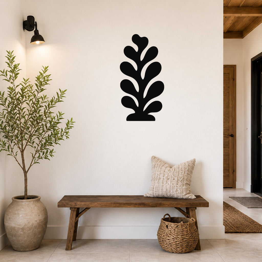 Black metal leaf wall art with layered cutout design, mounted on a white wall above a wooden bench in a entryway.