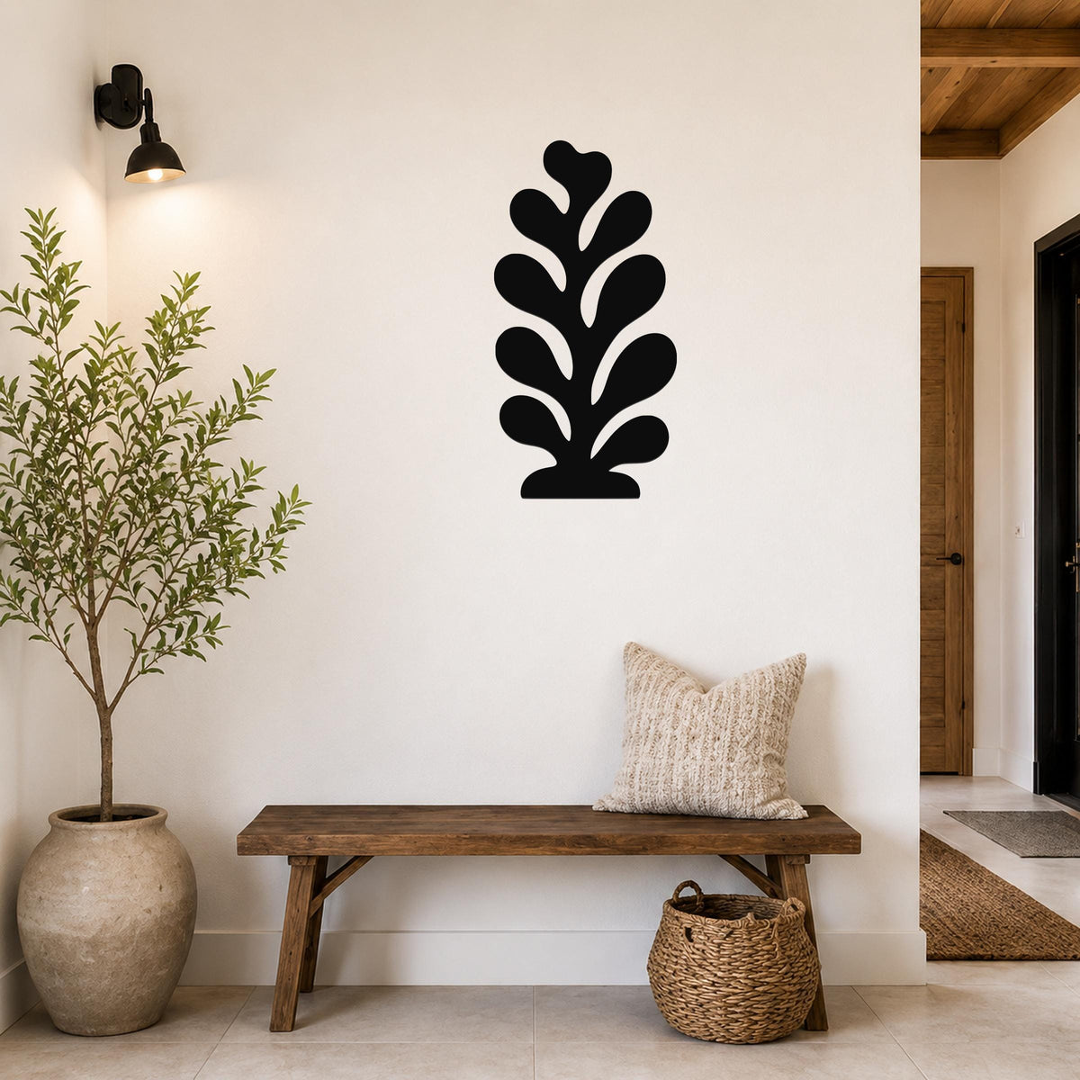 Black metal leaf wall art with layered cutout design, mounted on a white wall above a wooden bench in a entryway.