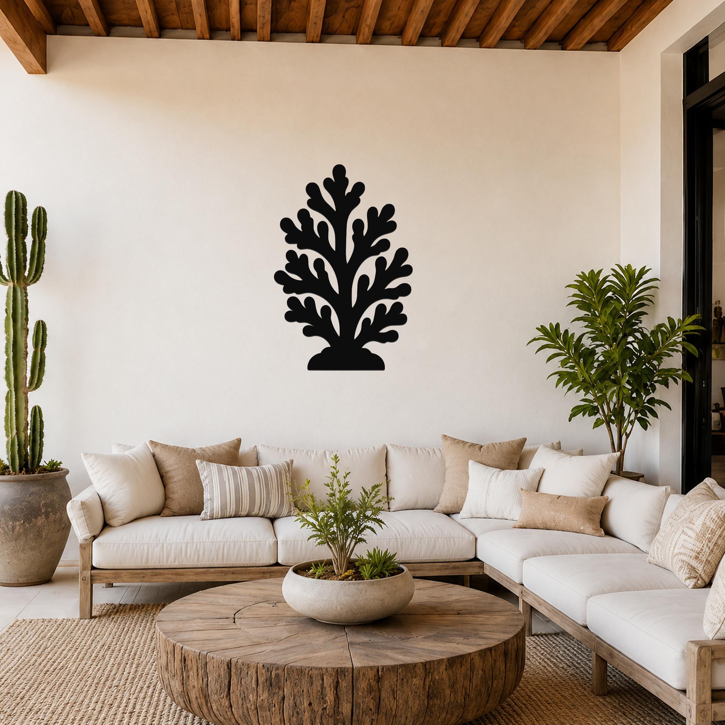 Black metal coral wall art with branching cutouts, mounted on a living room wall above a white sofa.