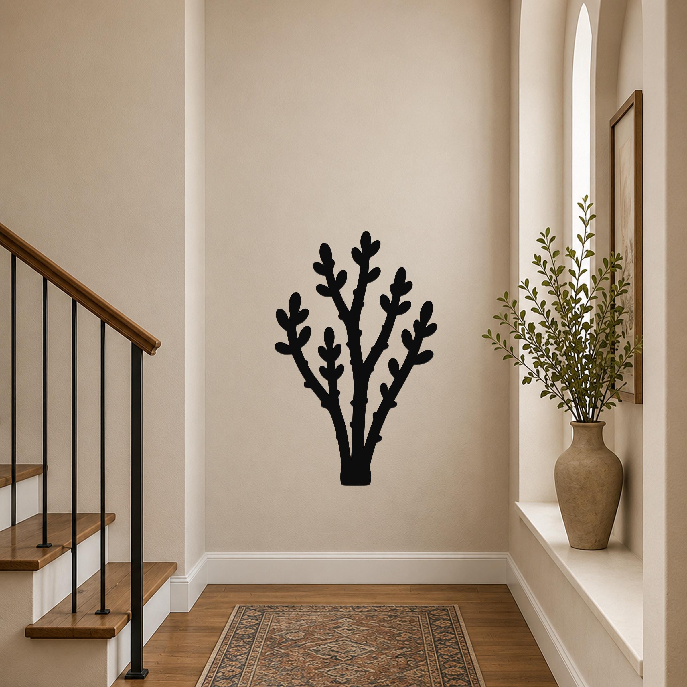 Black metal wall art in a desert branch silhouette design, mounted on a hallway wall above a patterned rug near a staircase.