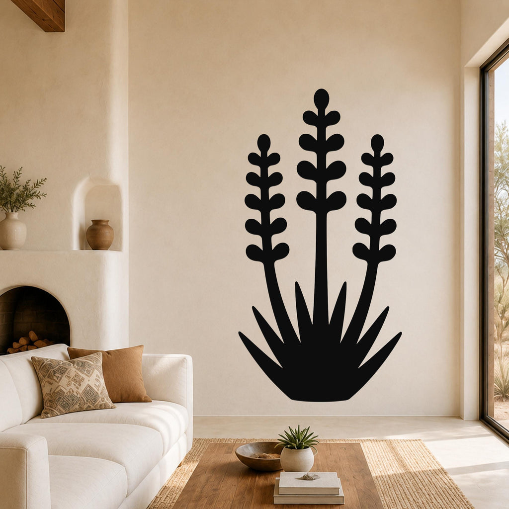 Black metal yucca wall art with layered leaf cutouts, mounted on a living room wall above a white sofa.