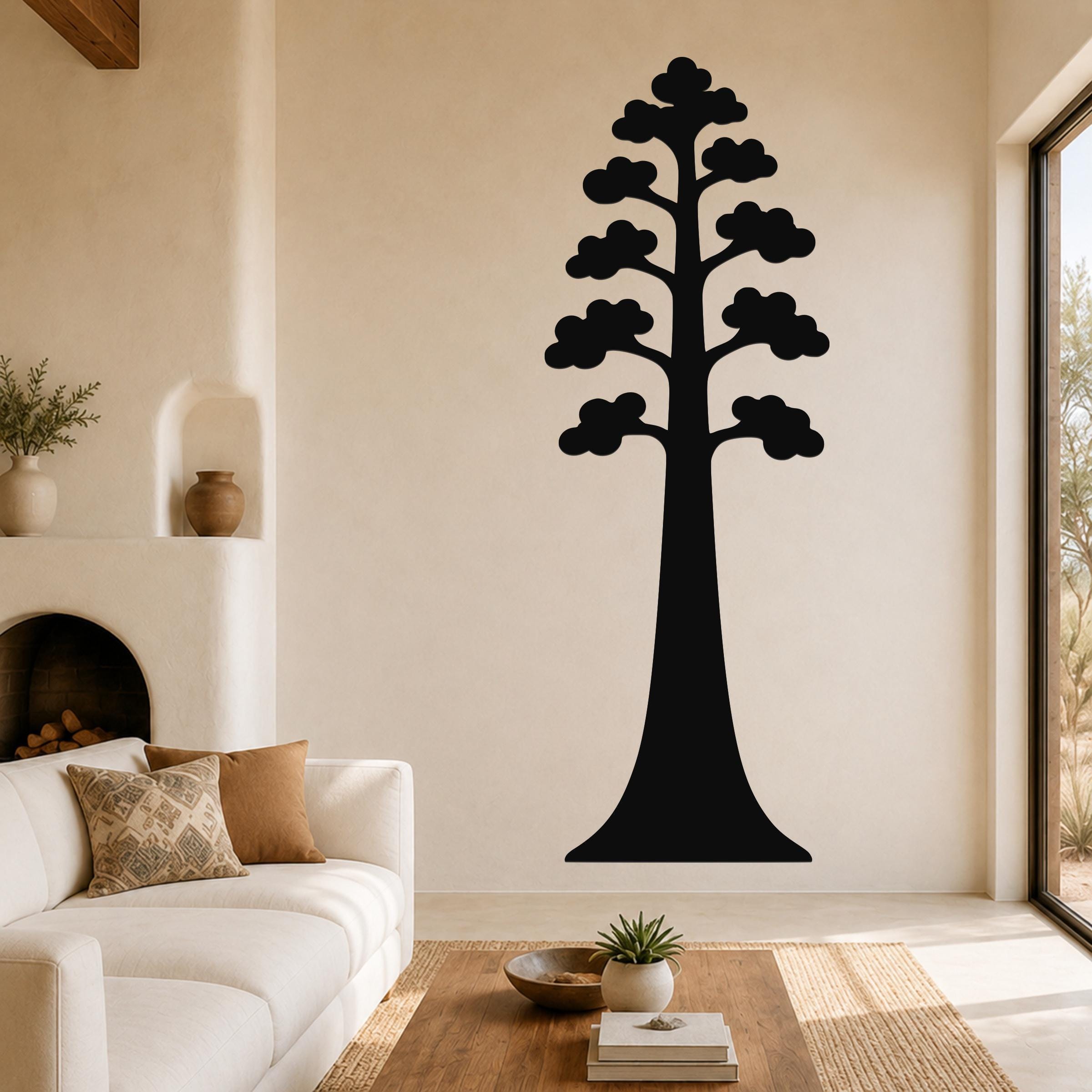 Black metal sequoia tree wall art with layered branch cutouts, mounted on a living room wall above a white sofa.